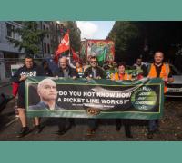 RMT members march, holding a banner that states "Do you know what a picket line is" alongside a photo of RMT General Secretary Mick Lynch